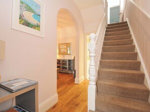 Eine Treppe mit Teppichstufen und weißen Spindeln, die zu einem Raum mit Holzboden und einem gerahmten Bild an der Wand führt.