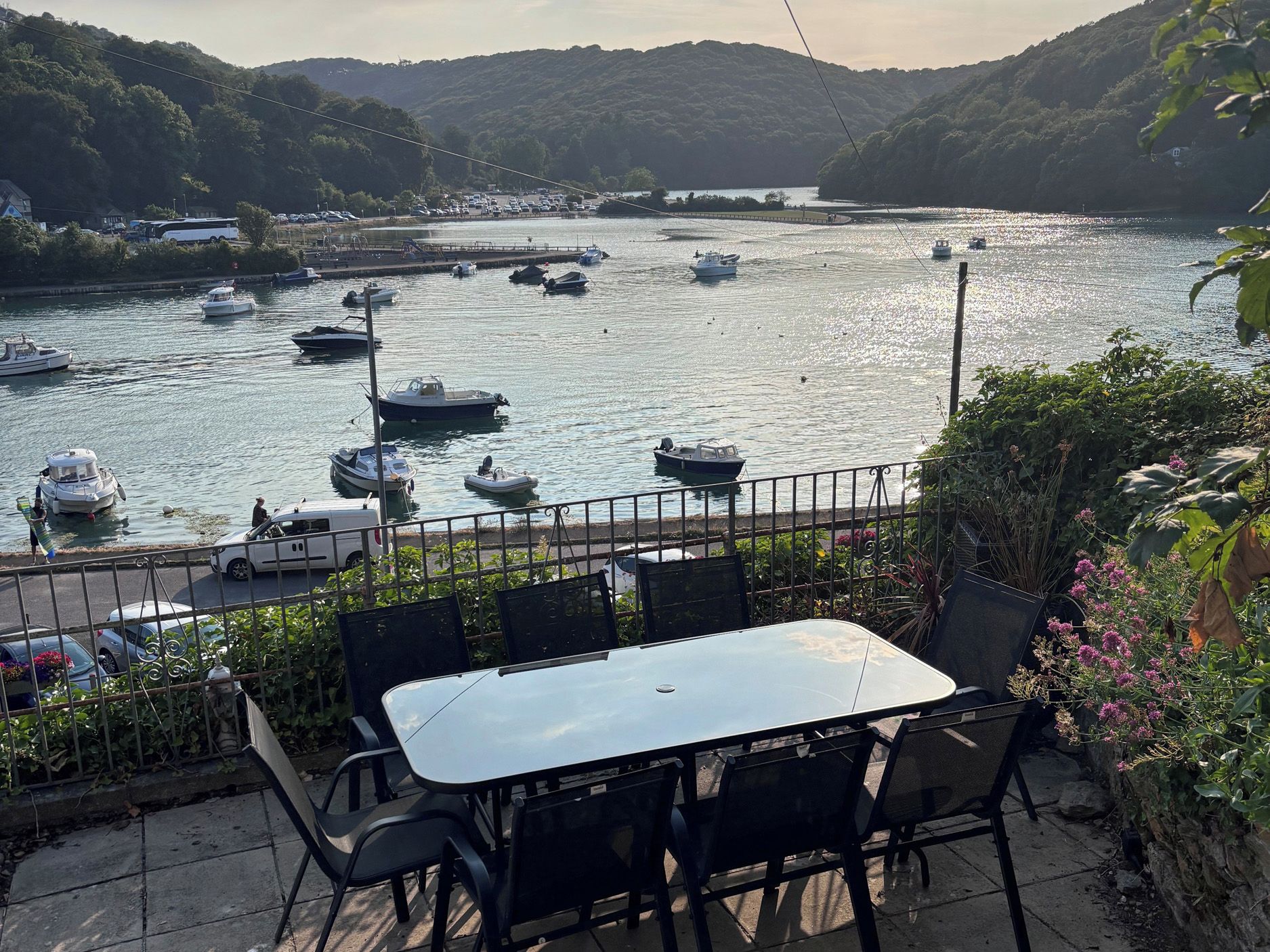 Vista al río con barcos, una mesa, sillas y una barandilla.