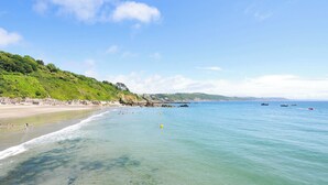 Ein Strand mit klarem Wasser, einem sandigen Ufer und einer grünen Hügelkette im Hintergrund.