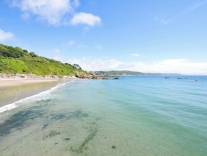 A beach with clear water, a sandy shore, and a green hillside in the background. - Overdale (Looe)