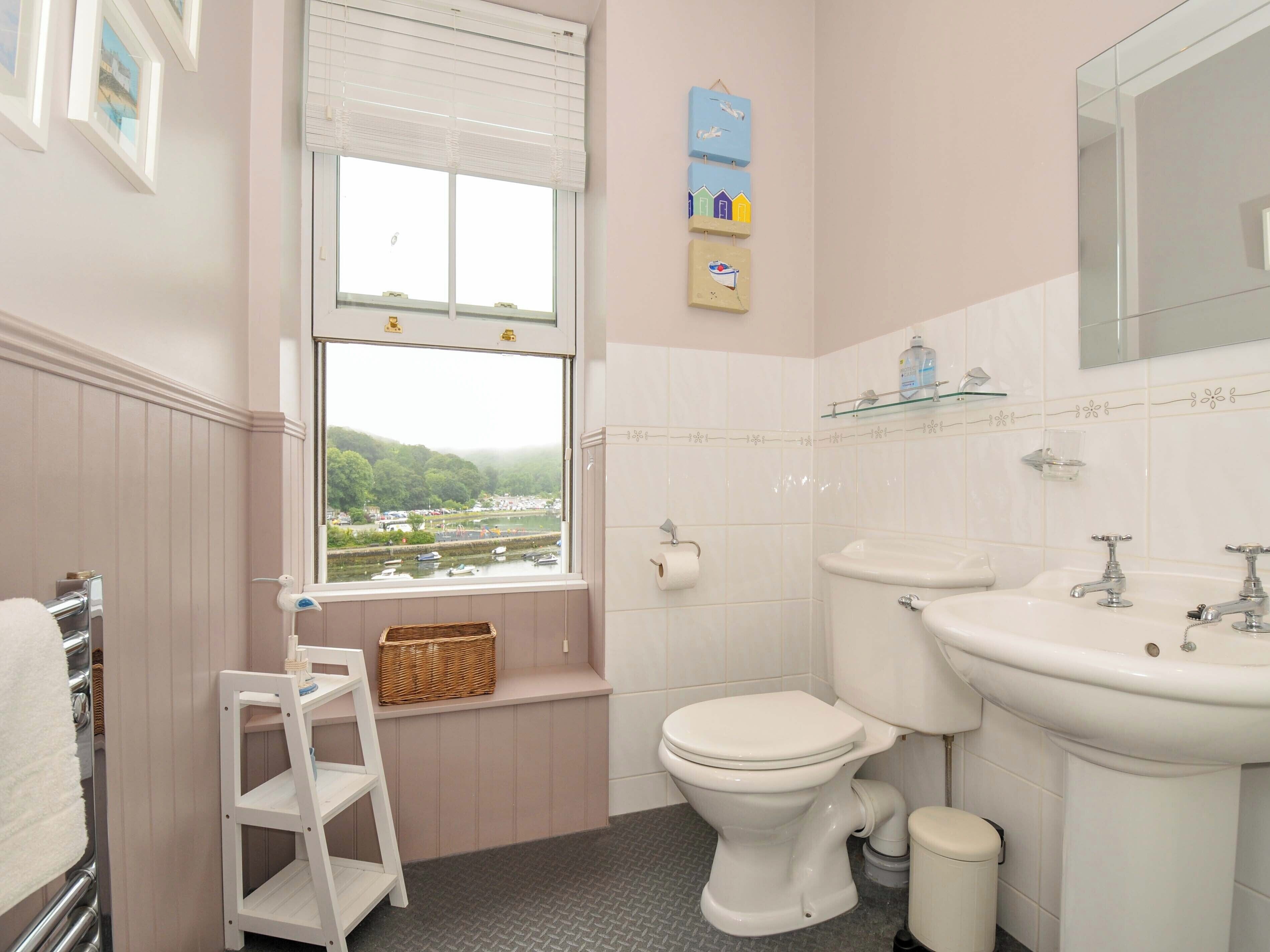 Une salle de bain avec des toilettes, un lavabo et une fenêtre donnant sur un lac et des bâtiments.