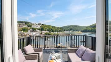A balcony with wicker furniture, a table with a croissant, and a view of a river and town.
