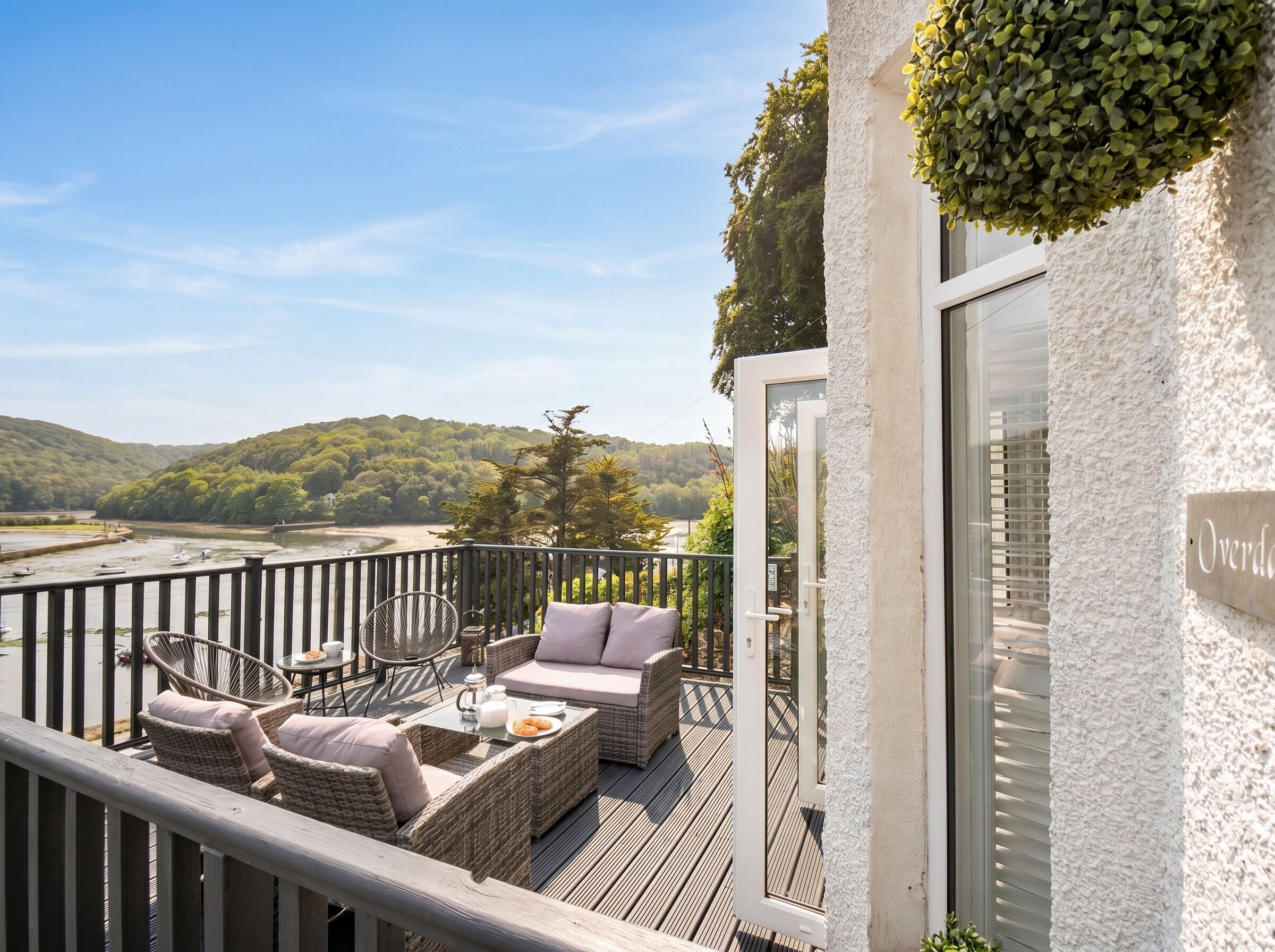 A balcony with wicker furniture, a glass door, and a view of a river and hills.