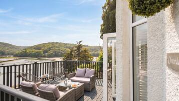 A balcony with wicker furniture, a glass door, and a view of a river and hills.
