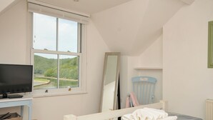 Ein Schlafzimmer mit einem Bett, einem Schreibtisch mit Computer, einem Fenster mit Blick ins Grüne und einem Spiegel.