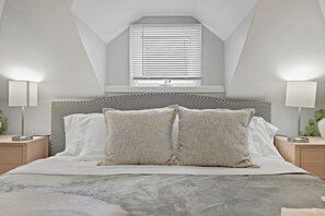 Una camera da letto con un letto, due abat-jour, una finestra con tende e un piccolo lucernario.
