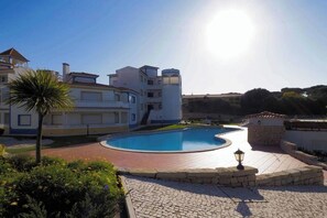 Un espace piscine comprenant une piscine aux formes arrondies, un palmier et un bâtiment doté de nombreux balcons.
