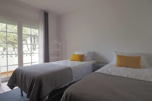 Une chambre d’hôtel avec deux lits, une table de chevet, une fenêtre donnant sur un beau paysage et un balcon.