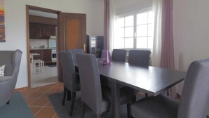 Un coin repas avec une table et des chaises, une cuisine à l’arrière-plan et une fenêtre avec des rideaux.