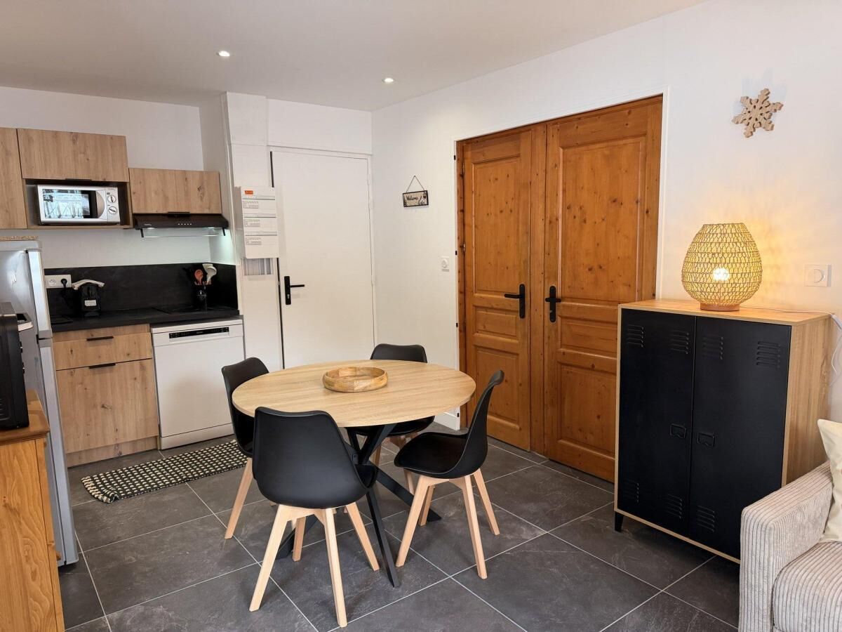 Een compacte keuken met moderne apparatuur, een eethoek met een ronde tafel en stoelen, en een uniek ontworpen garderobe.