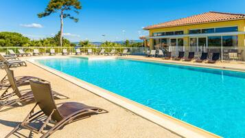 A swimming pool with lounge chairs, a building with a tiled roof, and a tree in the background.