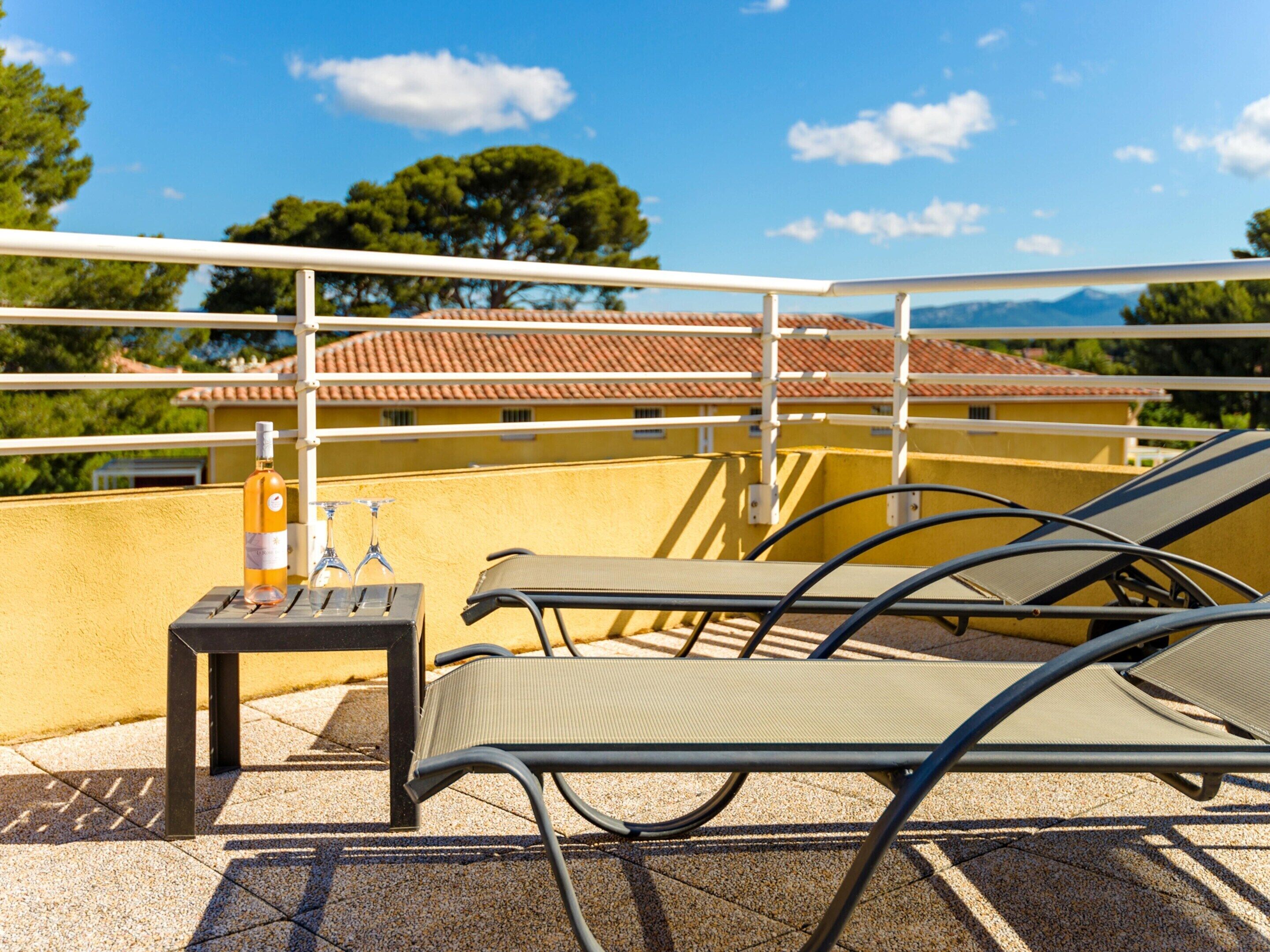 En tagterrasse med et bord, to loungesenge, en vinflaske og vinglas.