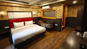 Quarto de hotel com cama grande, escrivaninha, cadeira, ventilador de teto e televisão na parede.