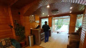 Interior de madeira com uma mesa de recepção, um sofá, uma lixeira e um vaso de plantas.