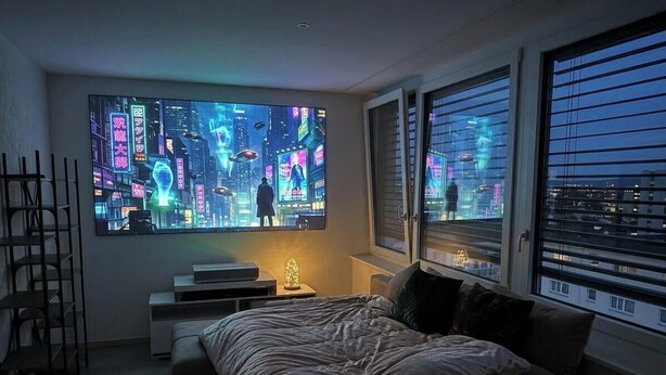 A bedroom with a large digital display on the wall, a bed, a bedside table with a lamp, and a window with blinds. - Mirami Apartement with Private Parking and Basellandcards (Allschwil)
