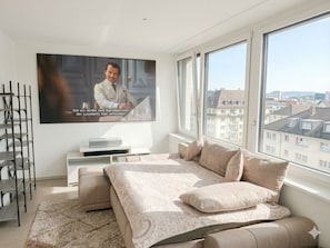 A bedroom with a bed, a TV, a window, and a view of buildings.