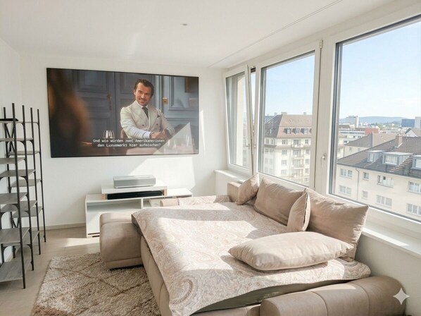 A bedroom with a bed, a TV, a window, and a view of buildings.