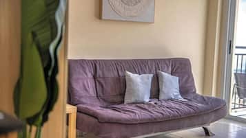 A purple sofa with cushions, a wooden chair, a large green plant, and a wall-mounted circular artwork.