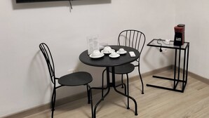 Huoneessa on seinälle asennettu taulutelevisio, pyöreä pöytä tuoleineen, kahvinkeitin sekä pieni pöytä, jossa on kuppeja ja aluslautoja.