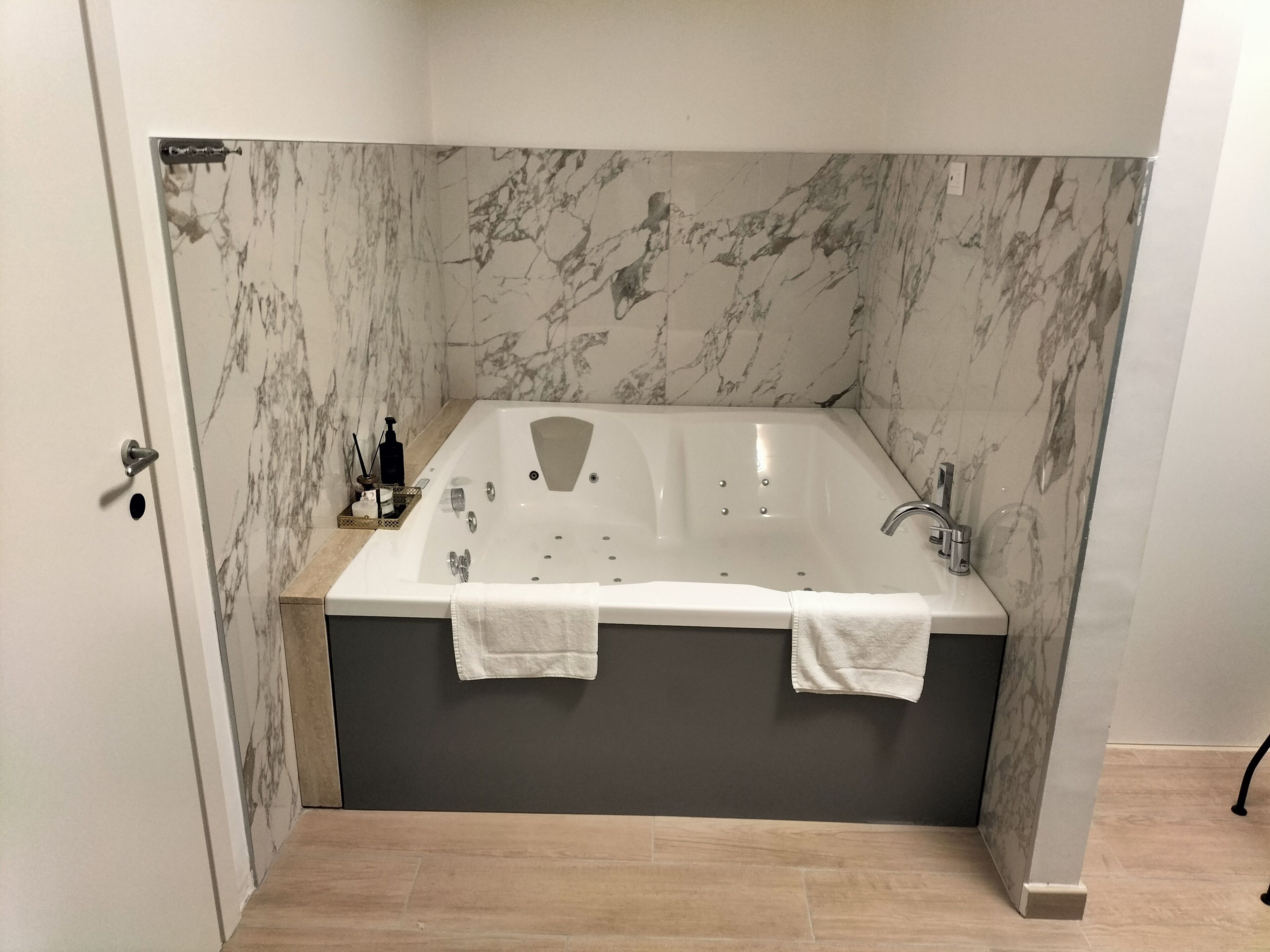 Un bagno moderno con una vasca freestanding, pareti in marmo e pavimento in legno.