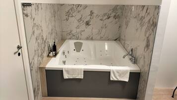 Un bagno moderno con una vasca freestanding, pareti in marmo e pavimento in legno.