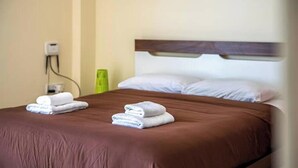 Ein Hotelzimmer mit einer braunen Bettdecke, zwei ordentlich gefalteten weißen Handtüchern, einem hölzernen Kopfteil und einer Steckdose.