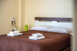 A hotel room with a brown bedspread, two neatly folded white towels, a wooden headboard, and a wall socket. - Peyia Pearl 27 – Sea View Studio w/ Large Veranda (Pegeia)