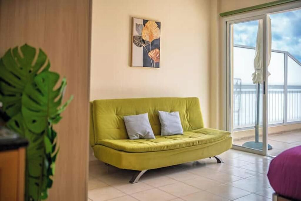 Ein Zimmer mit einem grünen Sofa, einem Bild an der Wand und einem großen Fenster mit Blick.