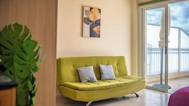 Ein Zimmer mit einem grünen Sofa, einem Bild an der Wand und einem großen Fenster mit Blick.