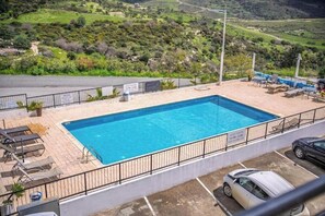 Ein rechteckiger Pool mit schwarzem Metallzaun, umgeben von Liegestühlen und einem Parkplatz.