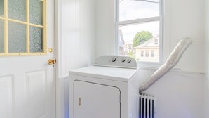 Et vaskerum med en frontbetjent vaskemaskine og tørretumbler, et vindue og en ventilationsslange.