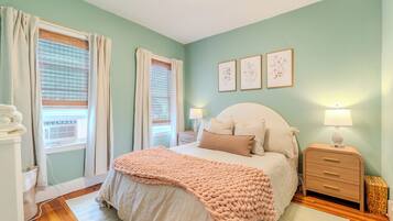 A bedroom with a bed, bedside tables, a nightstand, a window with curtains, and wall art.