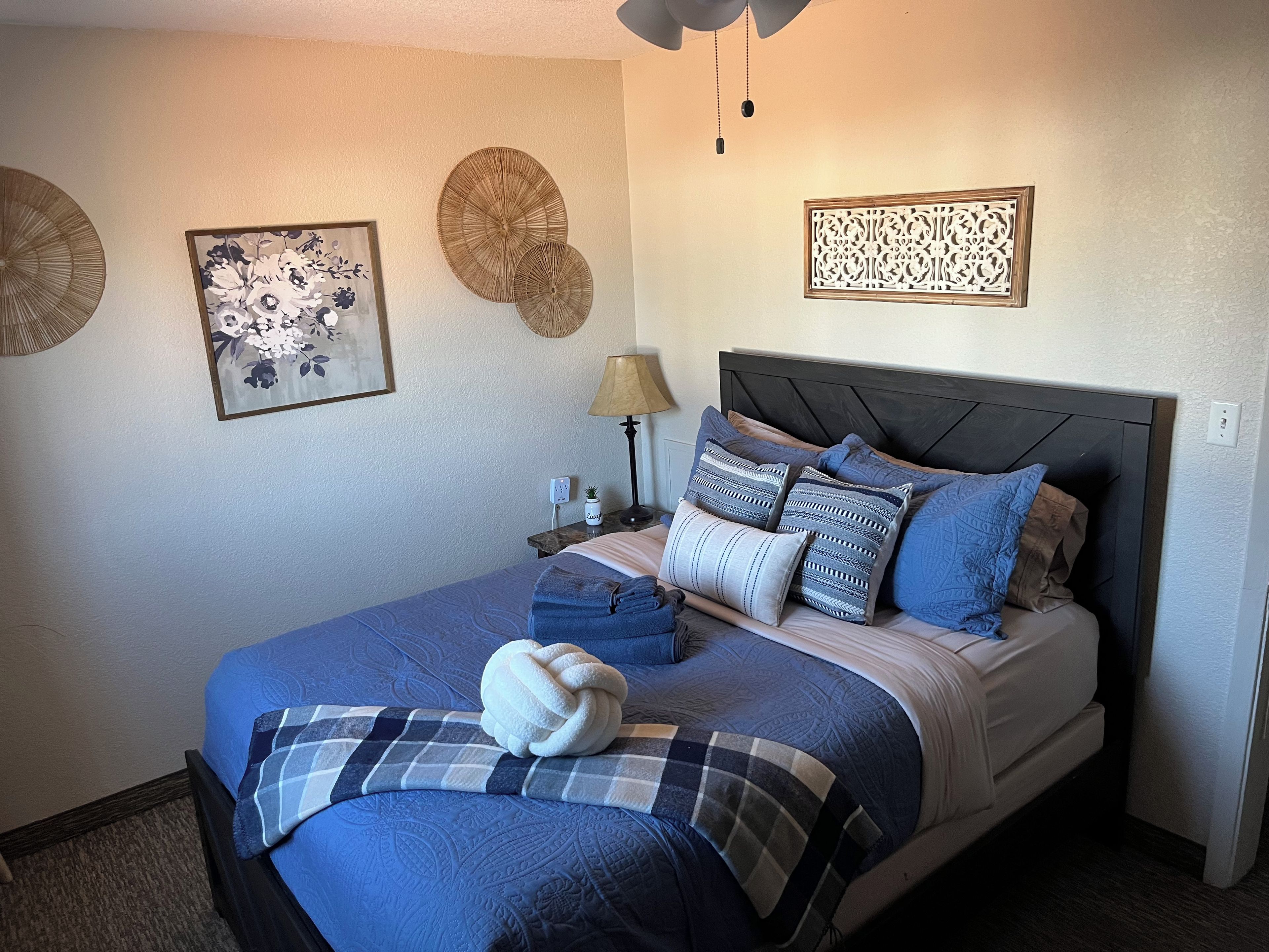 Een keurig opgemaakt bed met een blauw-wit geruit plaid, een witte handdoek en meerdere kussens in blauw- en wit tinten.