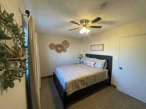 Ein Schlafzimmer mit einem Bett, einem Deckenventilator, einer Wandplatte und einer Tür.