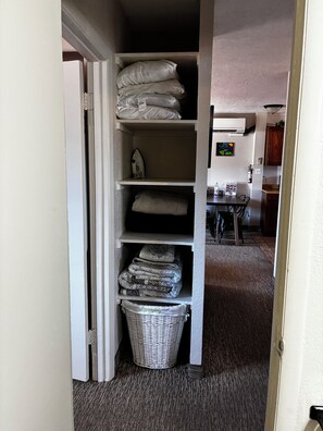 A storage closet with shelves containing folded blankets and pillows, a laundry basket, and a small house-shaped object. - Serene 2-bedroom apartment with AC in charming Page (Page)