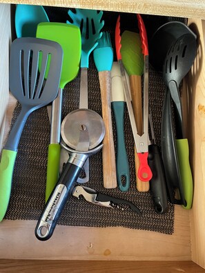 A drawer with kitchen utensils including spatulas, a grater, and a can opener.