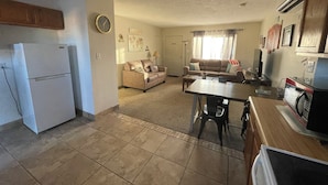 A living room with a sofa, a dining table, and a kitchen area with a refrigerator.