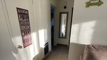 A hallway with a carpeted floor, a door with a motivational poster, a mirror, and a couch with patterned cushions.