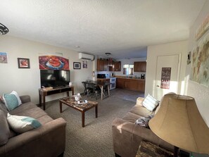A living room with a TV, sofa, coffee table, and a kitchen in the background.
