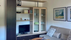 Ein modernes Wohnzimmer mit einem Holzesstisch, einem Fernseher, einer Couch und einer dekorativen Pendelleuchte.
