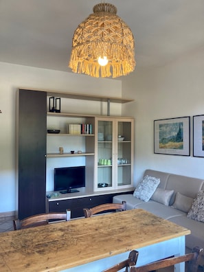 A modern living room with a wooden dining table, a television, a sofa, and a decorative hanging light fixture.