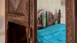 Ein hölzerner Kleiderschrank mit aufwendigen Schnitzereien und ein Spiegel, der ein Bett mit blauer Bettdecke reflektiert.