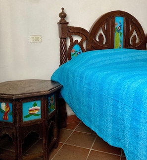 A wooden bed with a blue bedspread and a nightstand with painted designs.
