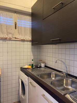 Eine Küche mit Waschmaschine, zwei Spülen und einem Fenster mit Vorhängen.