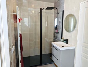 A modern bathroom with a glass-enclosed shower, a white sink with a mirror, and a red towel on a rack. - Vrbo Property (Lagord)