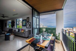 Ein modernes Wohnzimmer mit Essbereich, großen Fenstern und einem Balkon mit Blick auf die Stadt.
