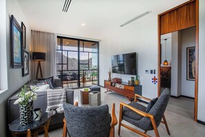 Ein modernes Wohnzimmer mit einer Couch, Sesseln, einem Fernseher und einem Balkon mit Blick.