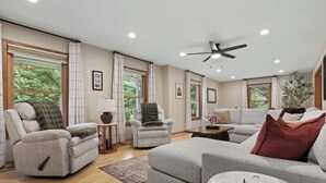 A spacious living room with a sofa, armchairs, a coffee table, and a ceiling fan.
