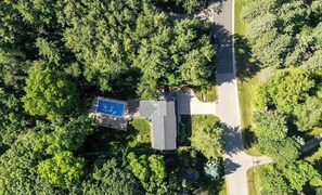 An aerial view of a residential area with a swimming pool, a house, and a road.