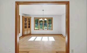 A room with a wooden floor, a built-in cabinet, a large window with a view of greenery, and a hanging light fixture. - Private Pool - Hot Tub - Sauna - Game Room - Pets (Sun Prairie)